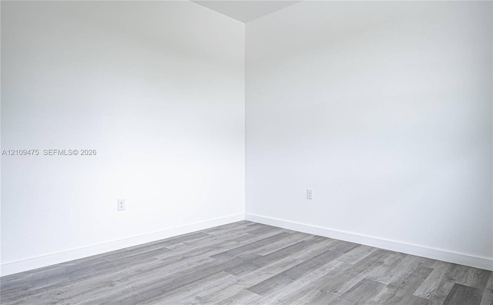 Neutral interior corner featuring smooth white walls and grey wood-finish flooring