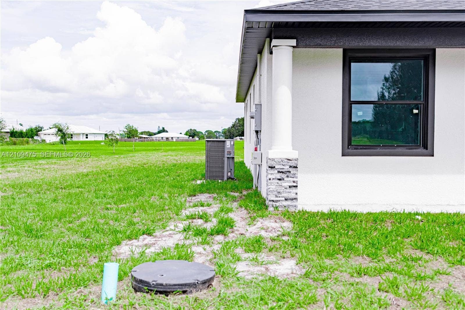 Stucco exterior featuring a decorative stone veneer column base, a crisp white structural pillar, and dark-trimmed window frames