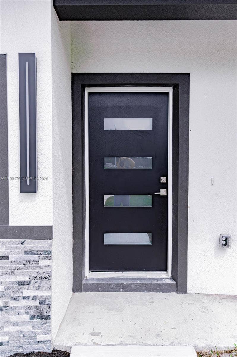 Modern black entry door featuring four horizontal glass inserts, brushed metal hardware, linear wall-mounted exterior lighting, and textured stone masonry detailing
