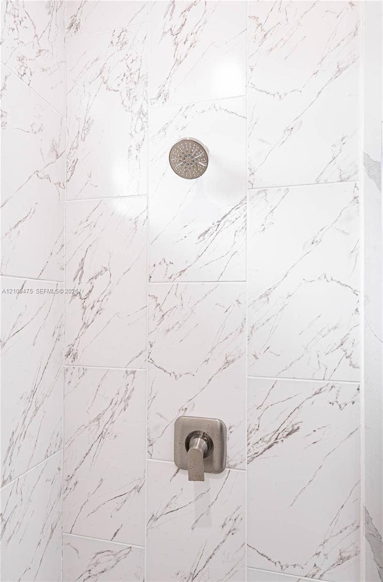 Shower enclosure featuring large-format veined tile walls, a brushed nickel rainfall showerhead, and a matching single-handle pressure-balance valve