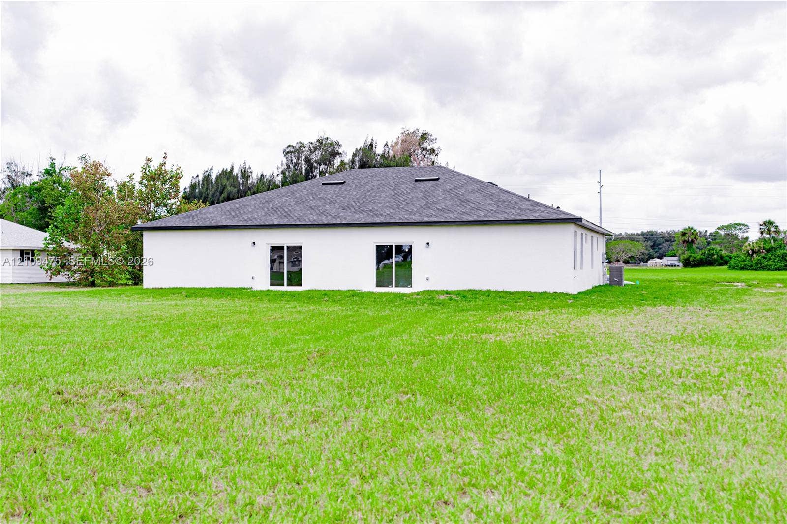 Single-story exterior featuring a white stucco facade, hip roof with integrated skylights, and two sliding glass doors opening to a large, open grass lot
