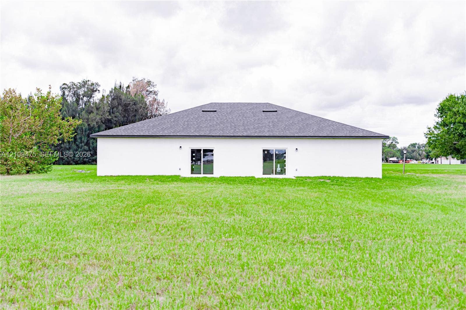 Exterior elevation featuring a light-toned smooth finish, hip roof with dark shingles, and dual glass sliding doors opening to an expansive grass yard
