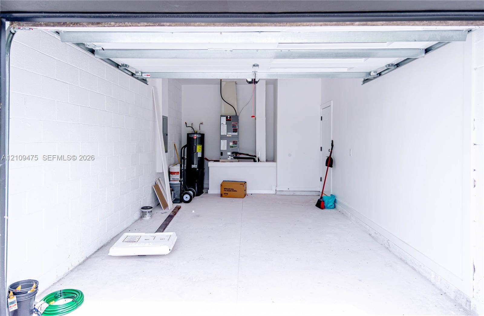 Enclosed garage featuring painted concrete block walls, concrete flooring, overhead door track system, and dedicated mechanical area with water heater