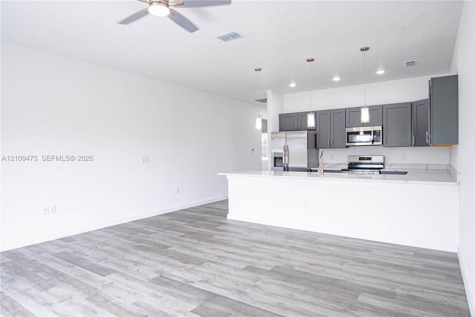 Kitchen featuring dark gray cabinetry, stainless steel appliances, a peninsula with stone-finish countertops, pendant lighting, and wood-finish flooring