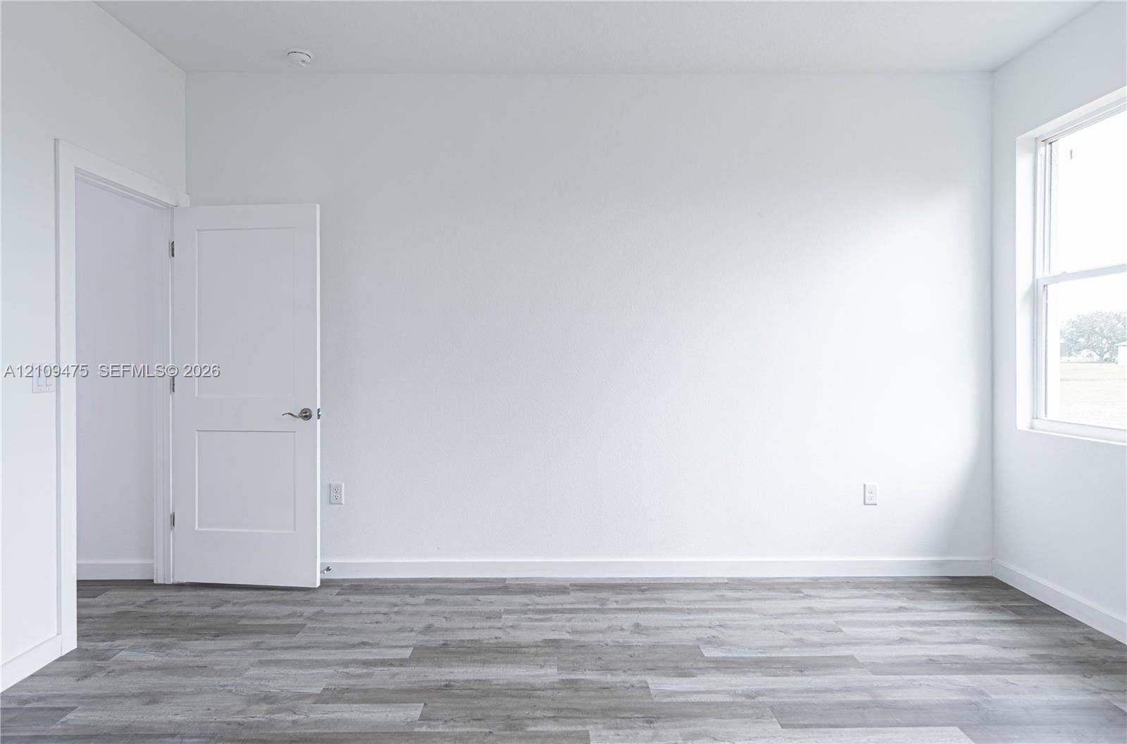 Interior room featuring wood-finish flooring, two-panel shaker style door, and a single-hung window