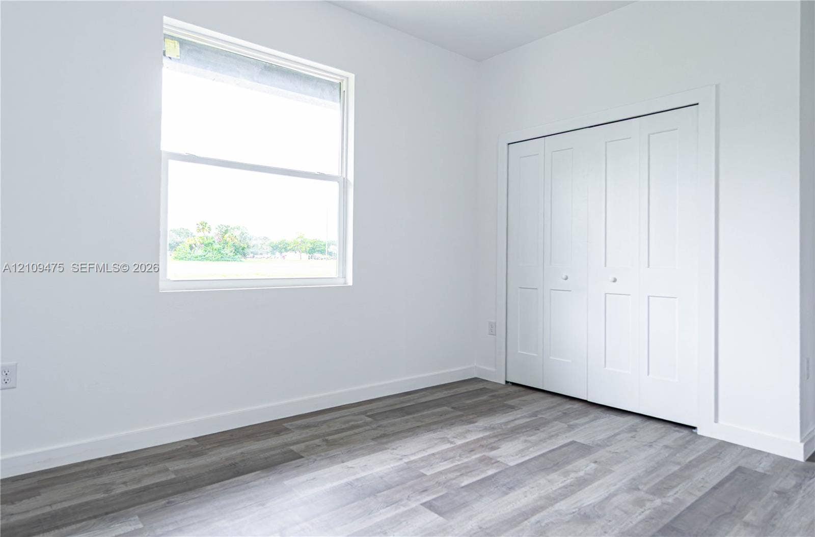 Room featuring wood-finish flooring, a single-hung window, and a built-in four-panel bifold closet door