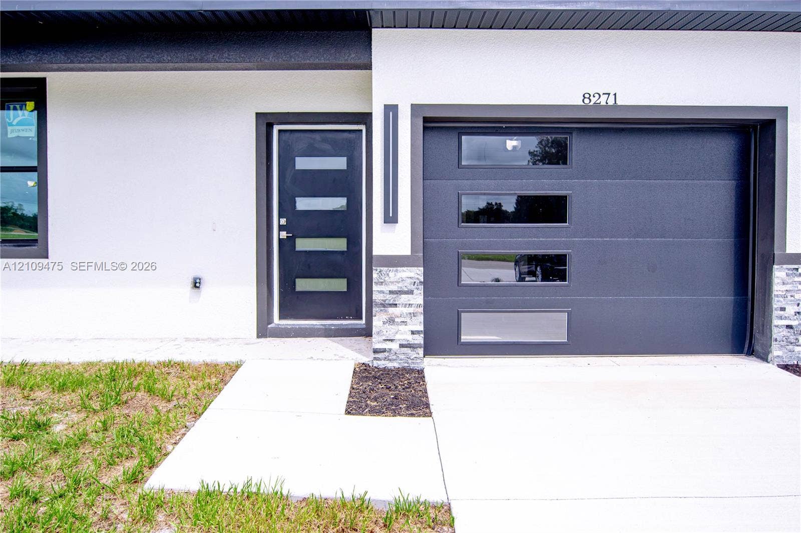 Modern exterior featuring a smooth white stucco facade, a dark metal garage door with horizontal glass panels, a matching entryway door with glass inserts, and stacked stone masonry accents