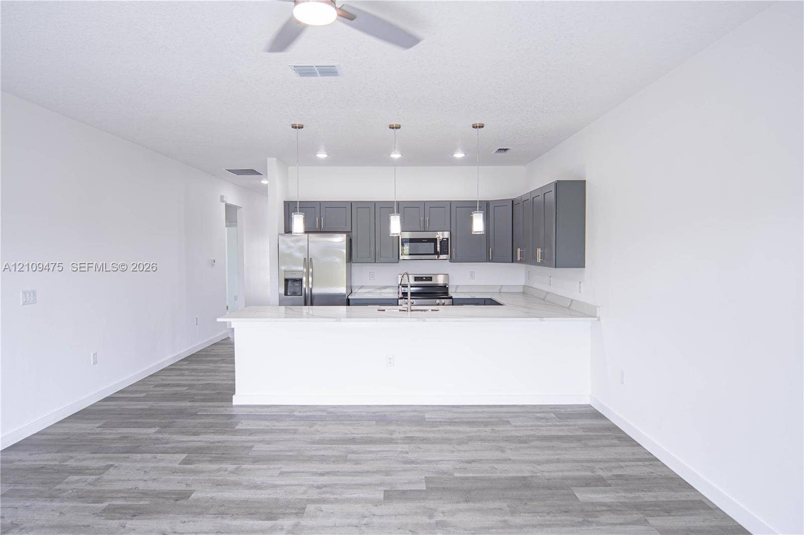 Kitchen featuring charcoal-toned cabinetry, light-toned countertops, stainless steel appliances, a breakfast bar, and wood-finish flooring