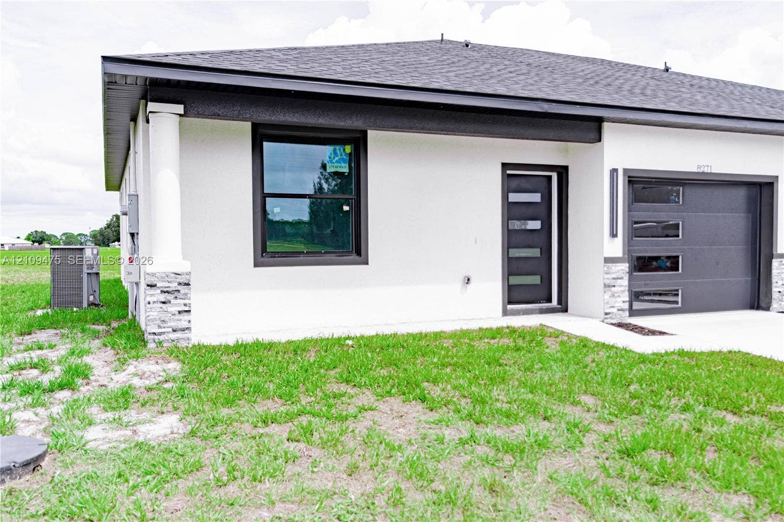 Modern exterior featuring a smooth stucco finish, stone veneer accents, a dark-toned sectional garage door with horizontal glass panels, and a matching entry door with inset windows