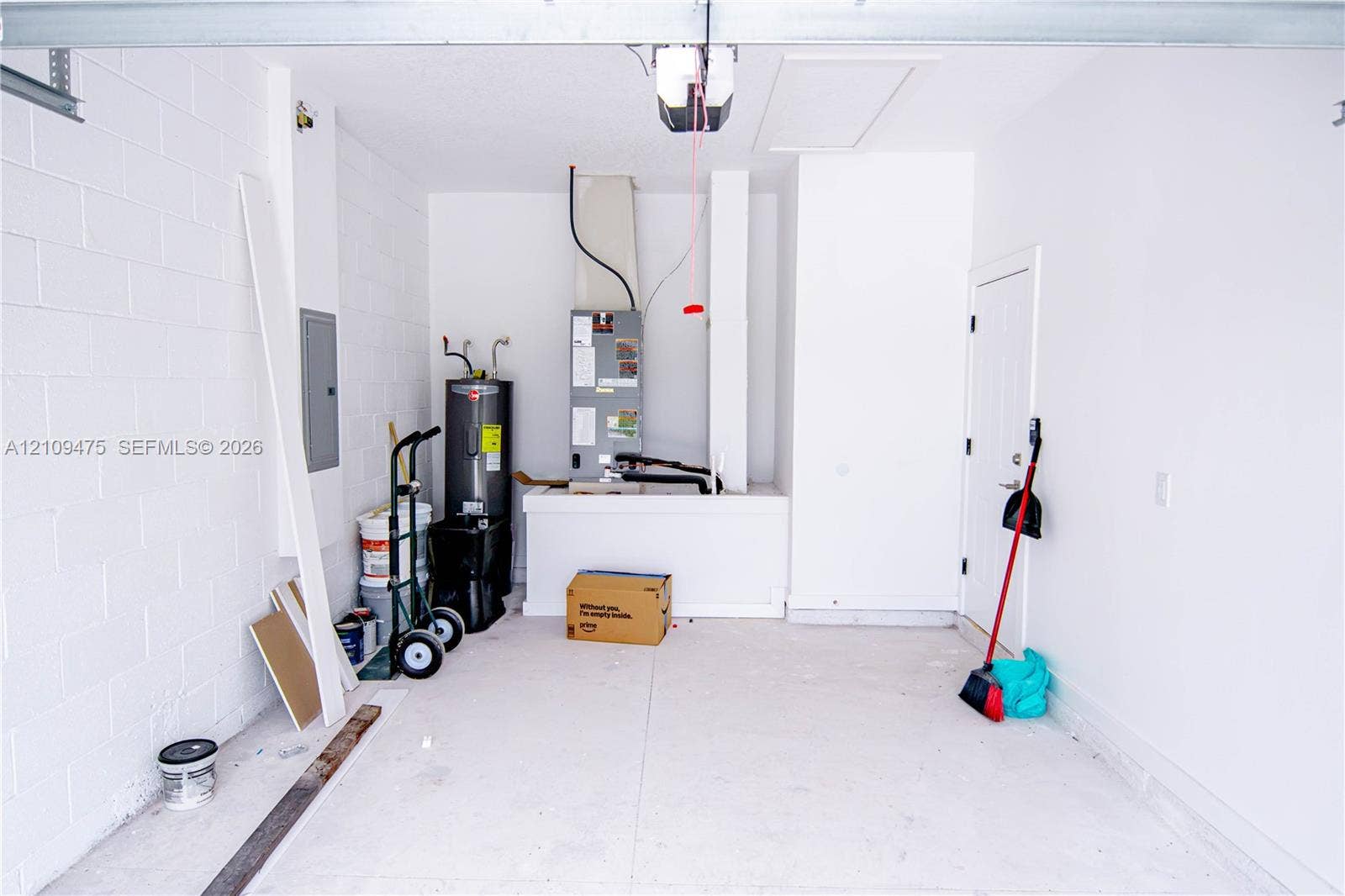 Garage space featuring painted concrete block walls, a concrete floor, an integrated electrical panel, and mechanical systems including a water heater and HVAC unit