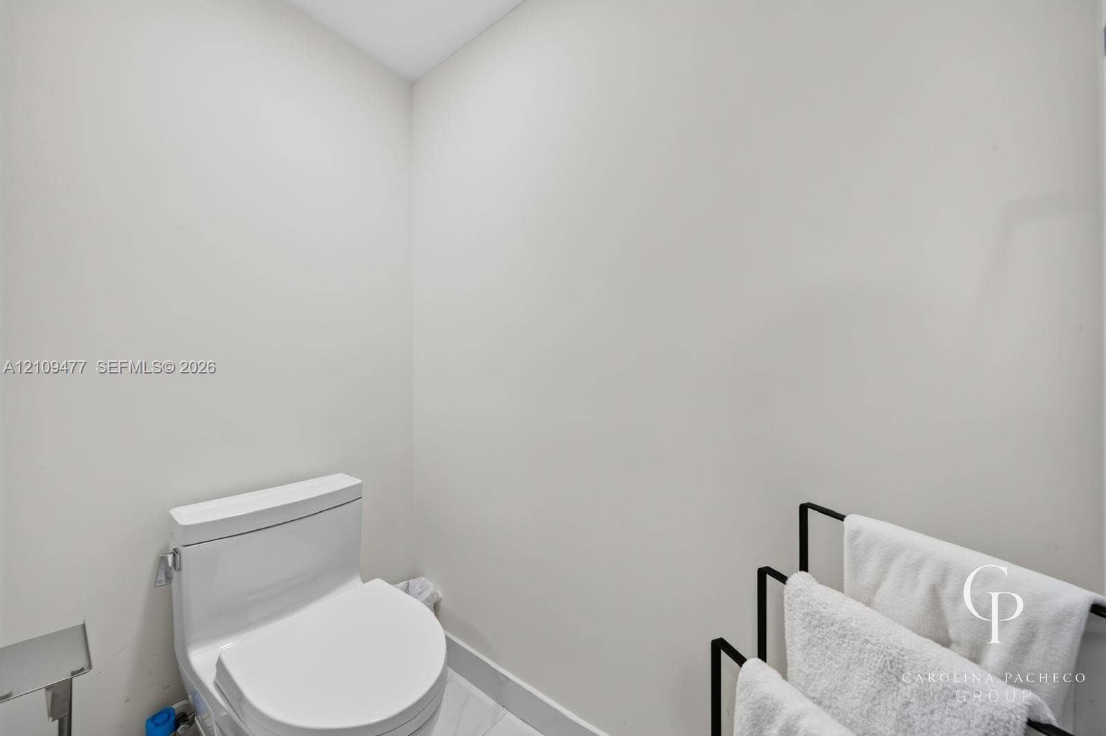 Modern white toilet with an elongated bowl and polished silver-tone hardware set against crisp neutral walls and stone-finish flooring