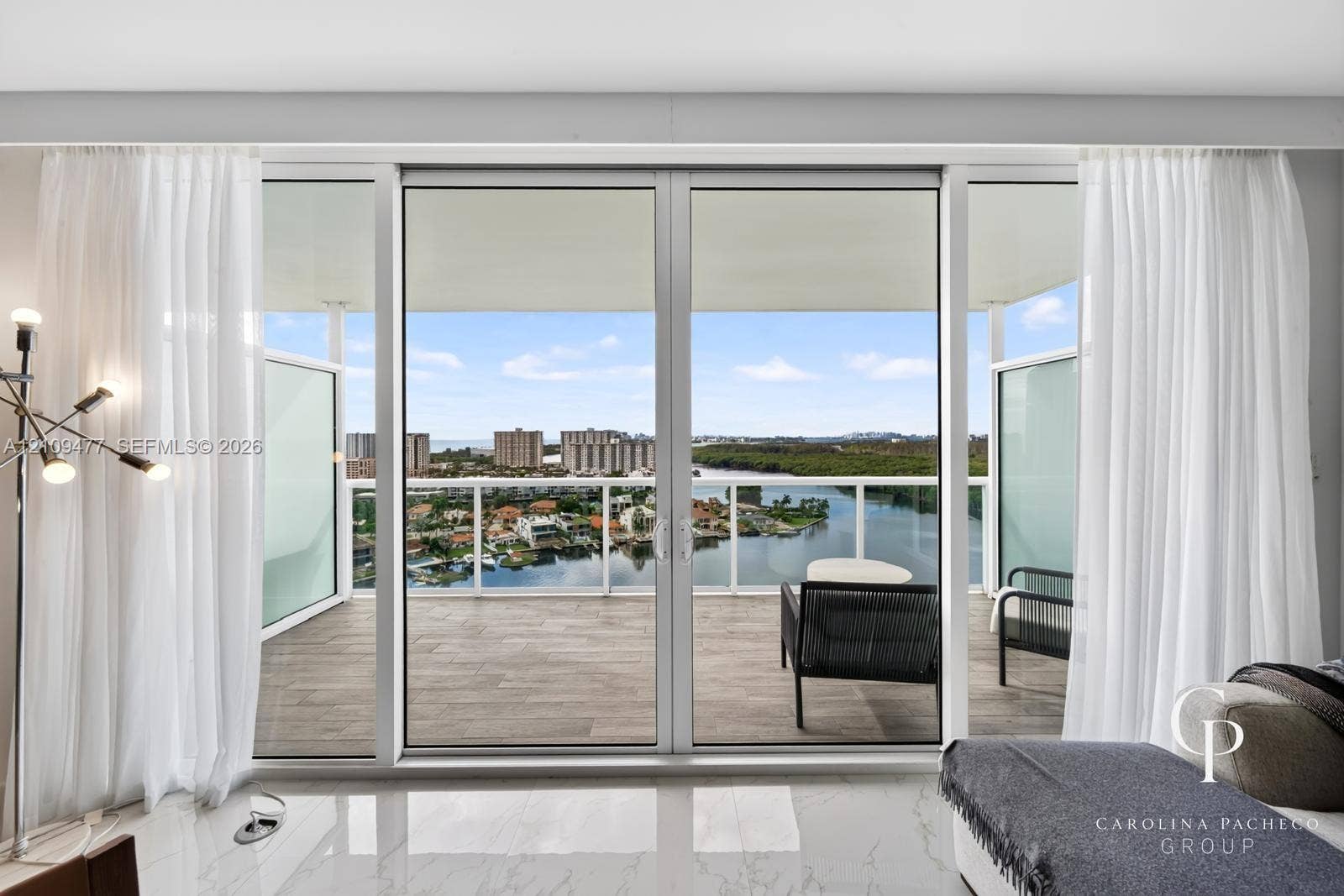 Floor-to-ceiling glass sliding doors opening to a covered balcony with tiled flooring and a glass panel railing