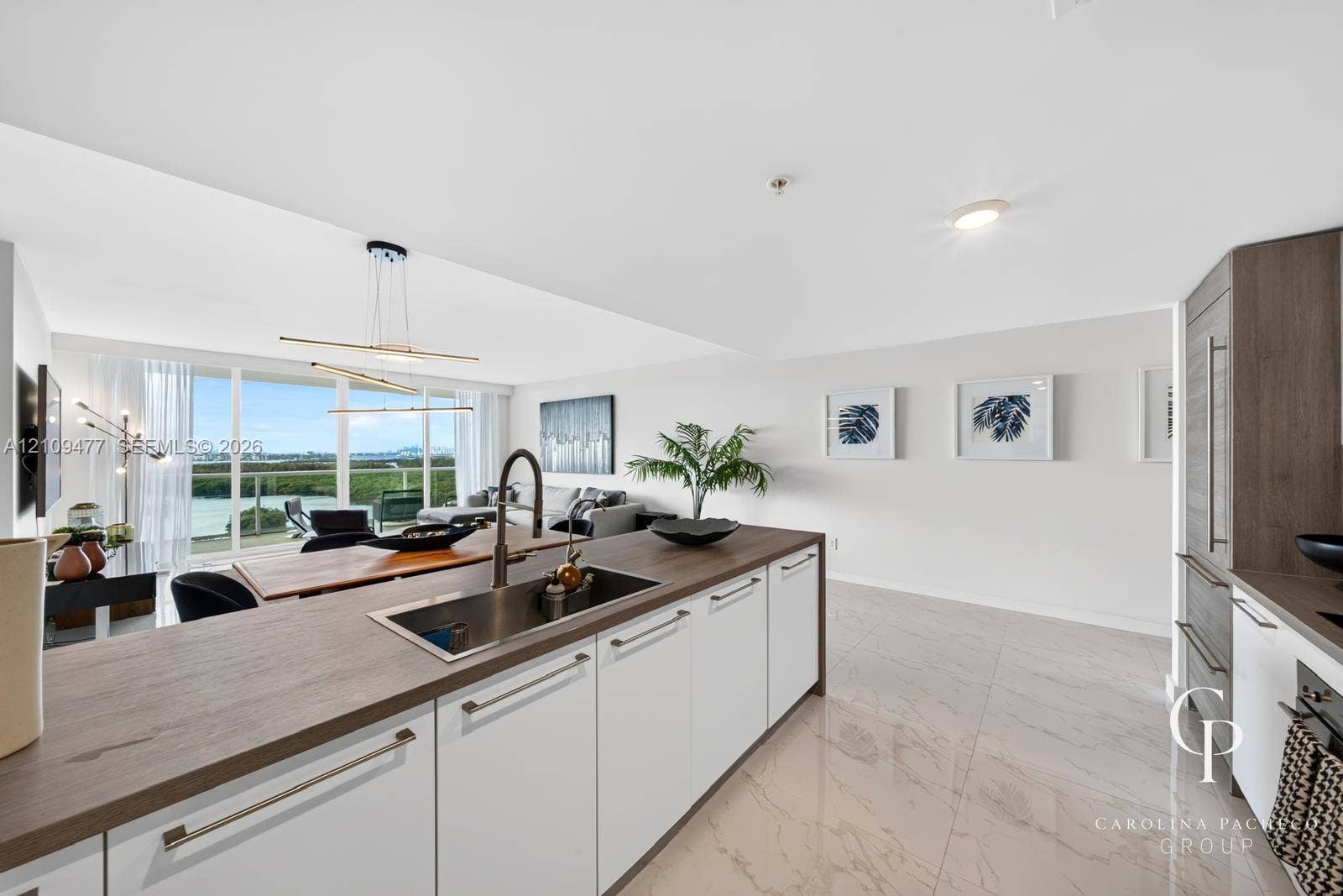 Kitchen featuring a central island with a wood-finish countertop, stainless steel undermount sink, high-arc faucet, white cabinetry with horizontal hardware, and large-format tile flooring
