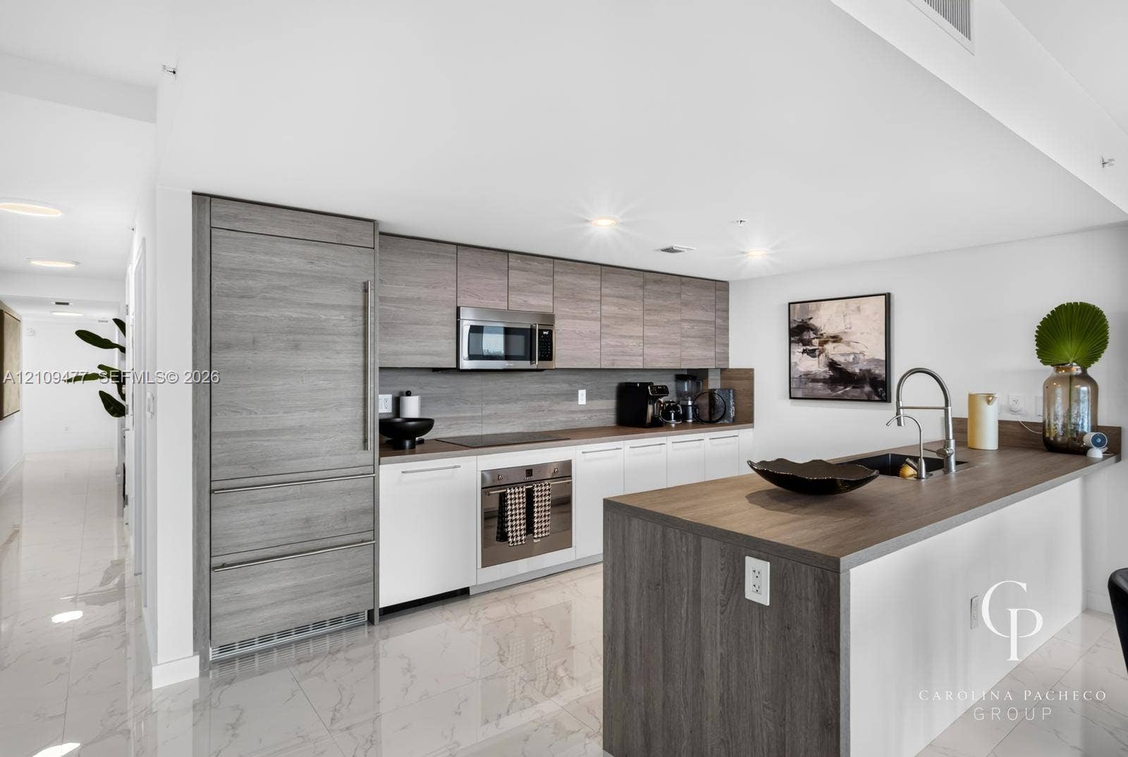 Contemporary kitchen featuring wood-finish cabinetry, a waterfall-edge kitchen island, integrated refrigerator, stainless steel appliances, and polished tile flooring
