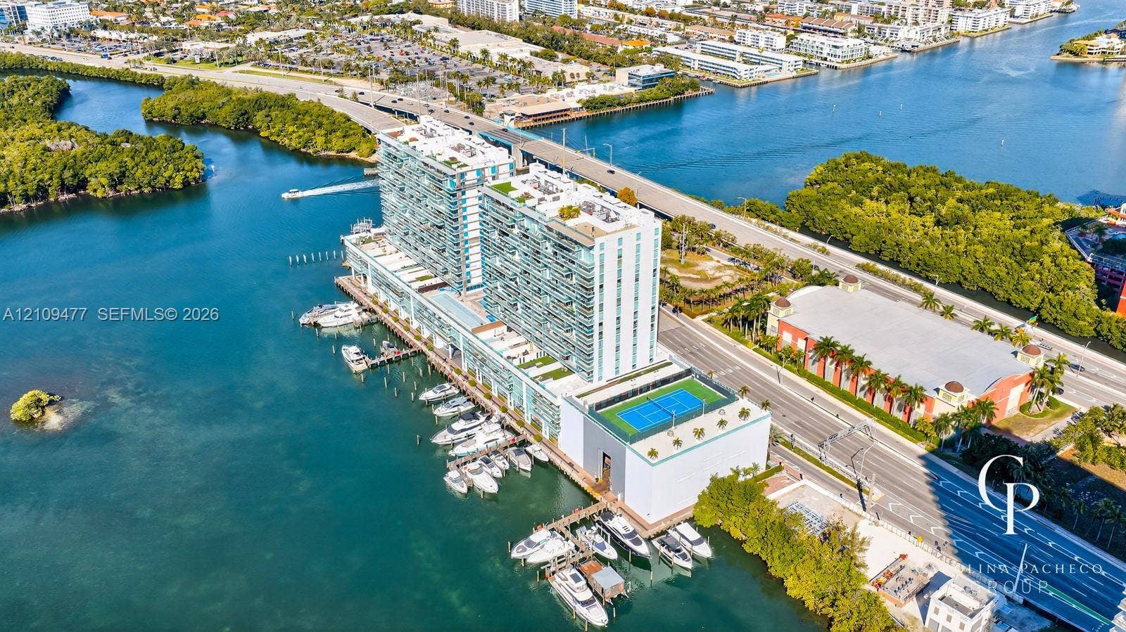 High-rise coastal property featuring deep-water marina slips, rooftop tennis court, expansive glass-paneled balconies, and manicured terrace landscaping
