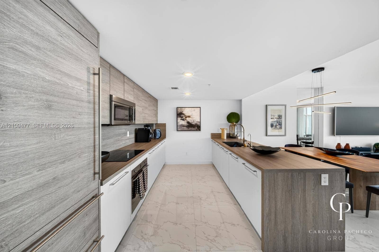 Kitchen featuring custom cabinetry with horizontal wood-grain finish, contrasting white lower cabinets, extended peninsula with wooden waterfall countertop, stone-finish tile flooring, and stainless steel built-in appliances