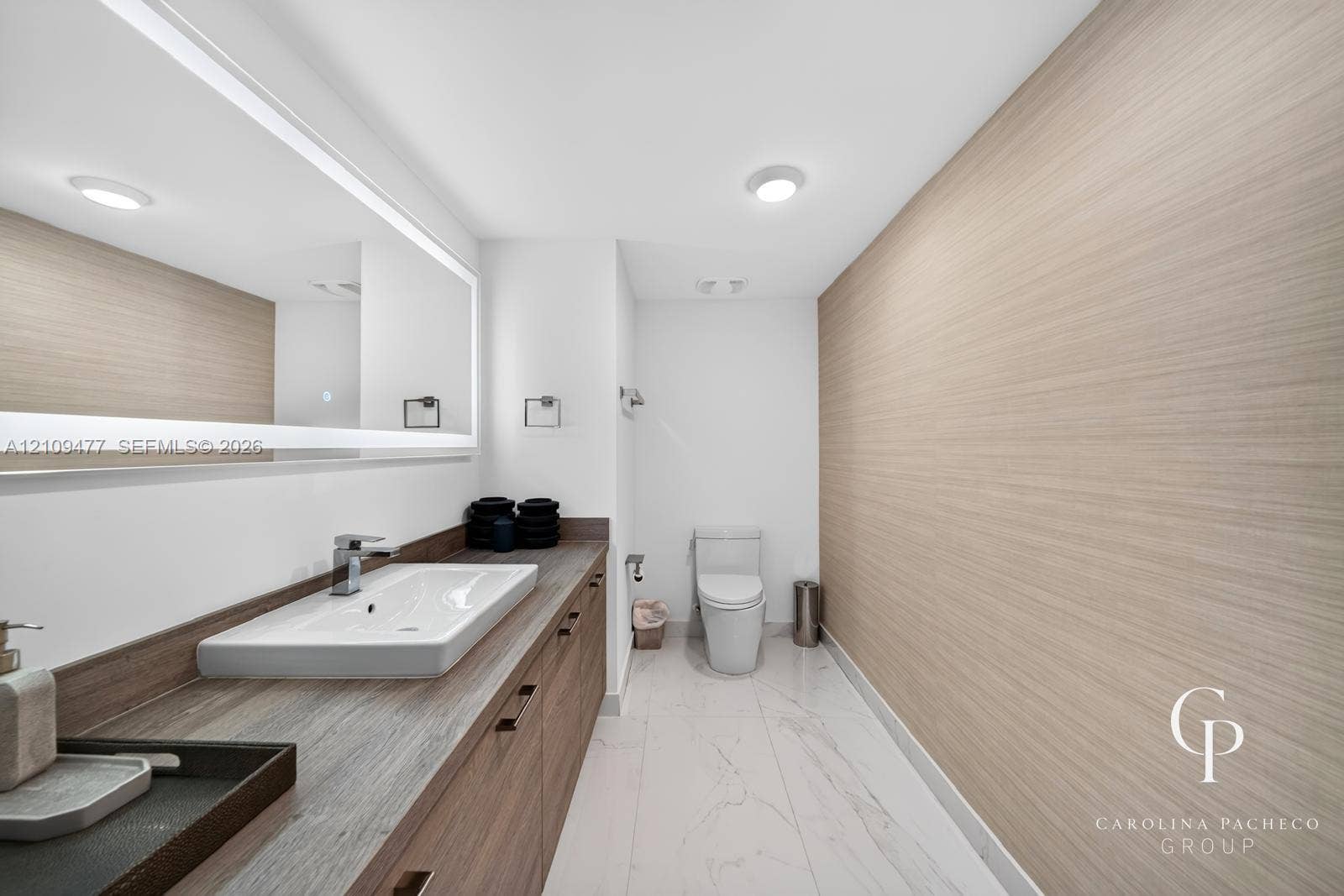 Bathroom featuring a wood-finish vanity with a rectangular vessel sink, integrated lighting mirror, stone-finish countertop, and large-format tile flooring