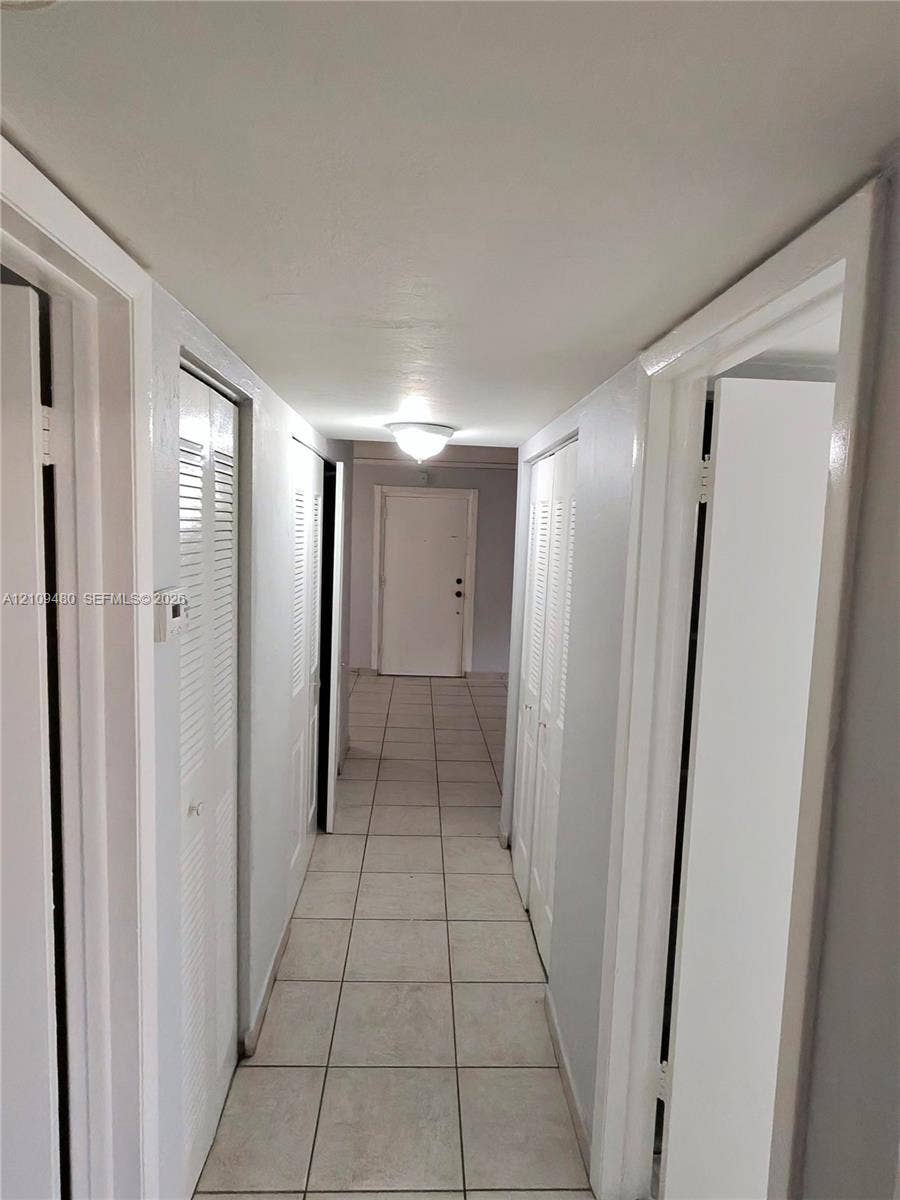 Neutral-toned tile flooring, multiple louvered-door closets, and a flush-mount ceiling fixture