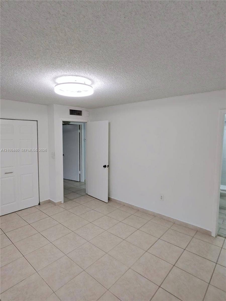 Neutral tile flooring, textured ceiling, flush-mount circular lighting, and paneled closet doors