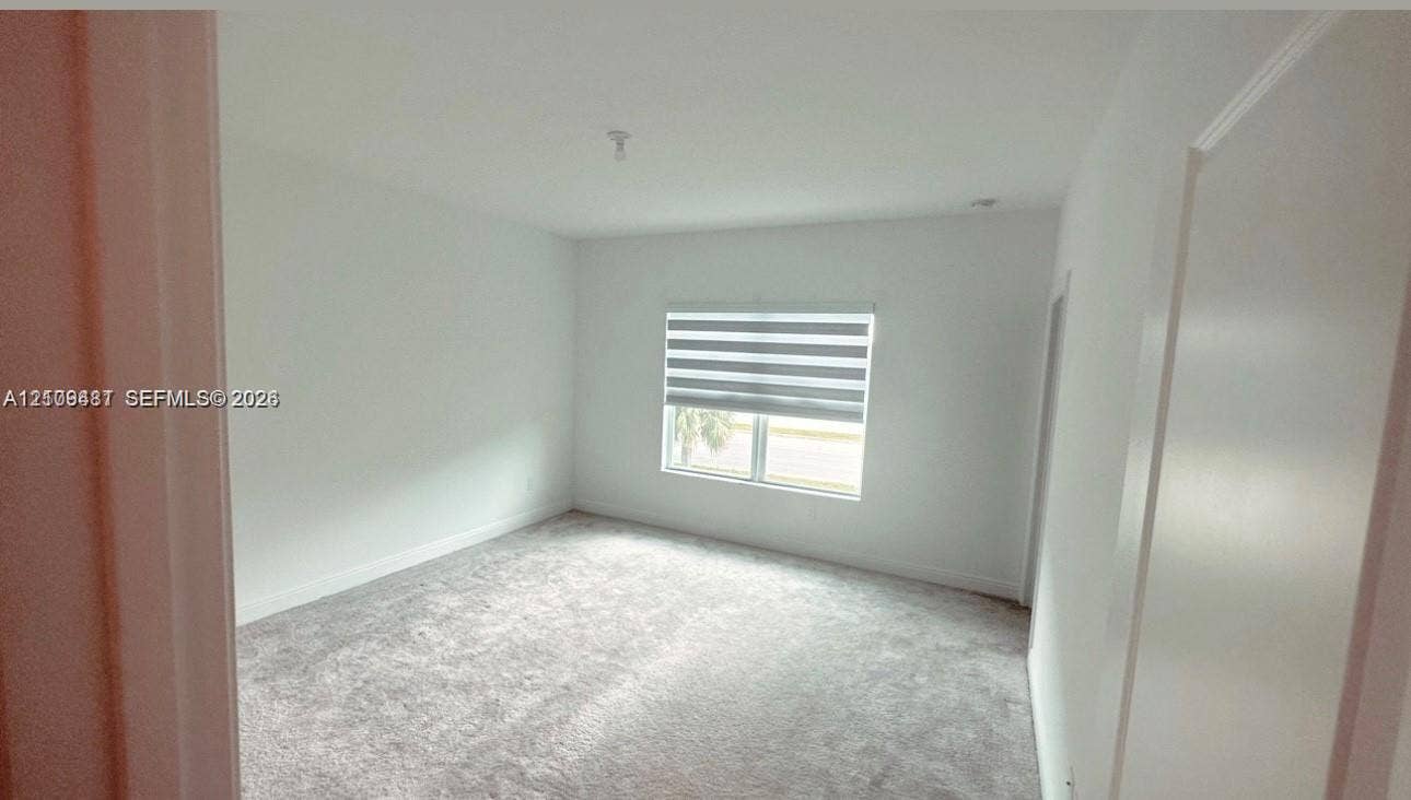Interior room featuring neutral wall paint, plush carpeting, and a window with installed roller shades