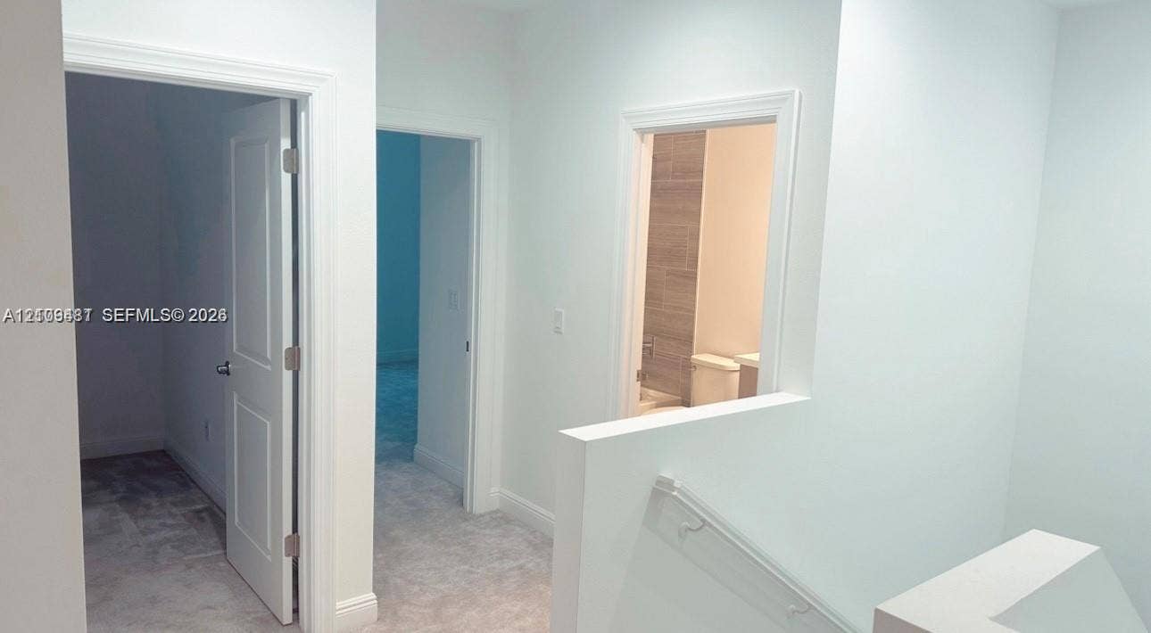 Interior hall featuring two-panel interior doors, light-toned carpeting, and a staircase with a wall-mounted handrail