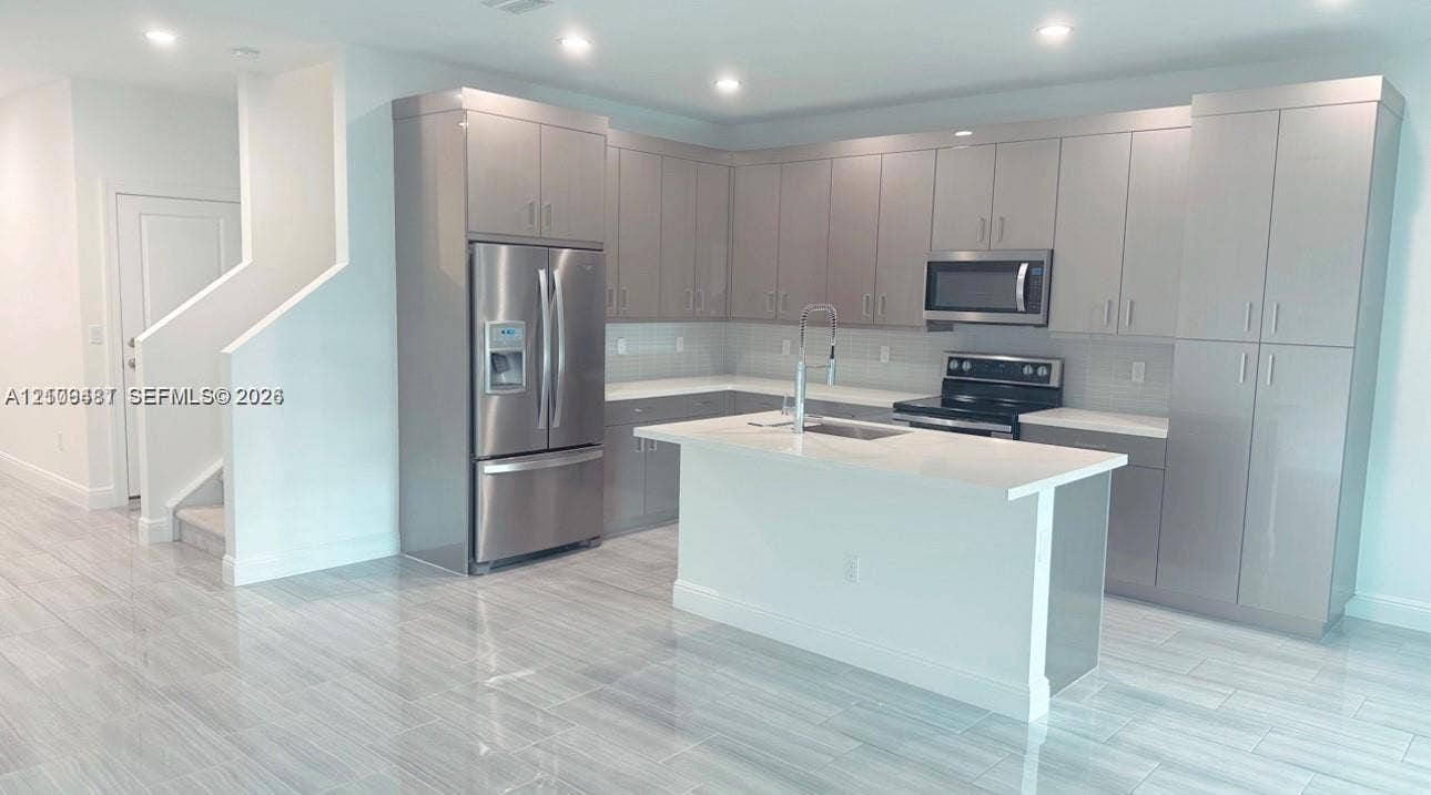 Kitchen featuring flat-panel cabinetry, a central island with a stone-surface countertop, stainless steel appliances, and large-format tile flooring