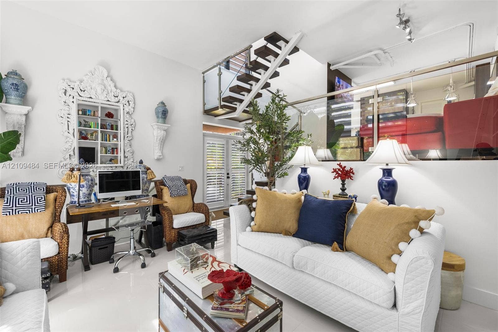 Open-concept interior featuring high ceilings, a floating staircase with glass railings, polished tile flooring, and integrated display shelving
