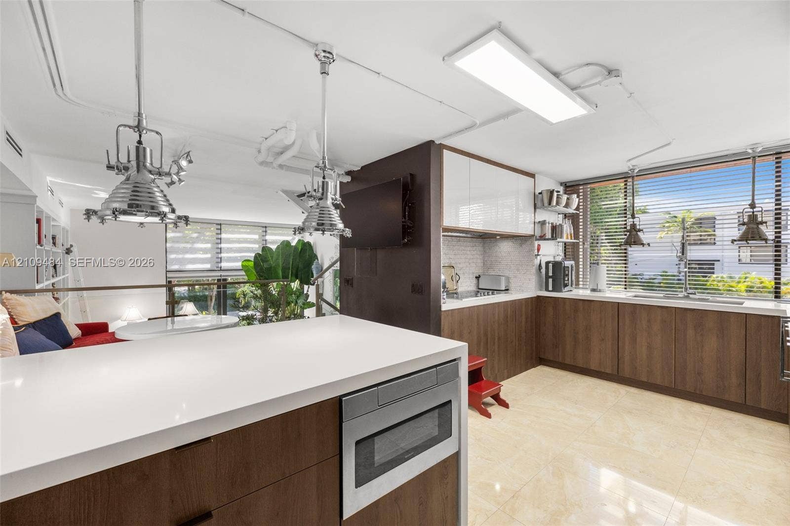 Kitchen featuring dual-toned cabinetry with high-gloss upper units and wood-finish lower units, light-toned stone-surface countertops, industrial-style pendant lighting, integrated microwave, and tiled flooring