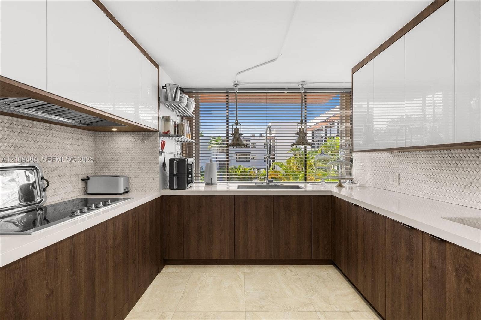 Kitchen featuring two-tone cabinetry with wood-finish lower units and high-gloss upper cabinets, solid-surface countertops, mosaic tile backsplash, and stainless steel undermount sink with pendant lighting