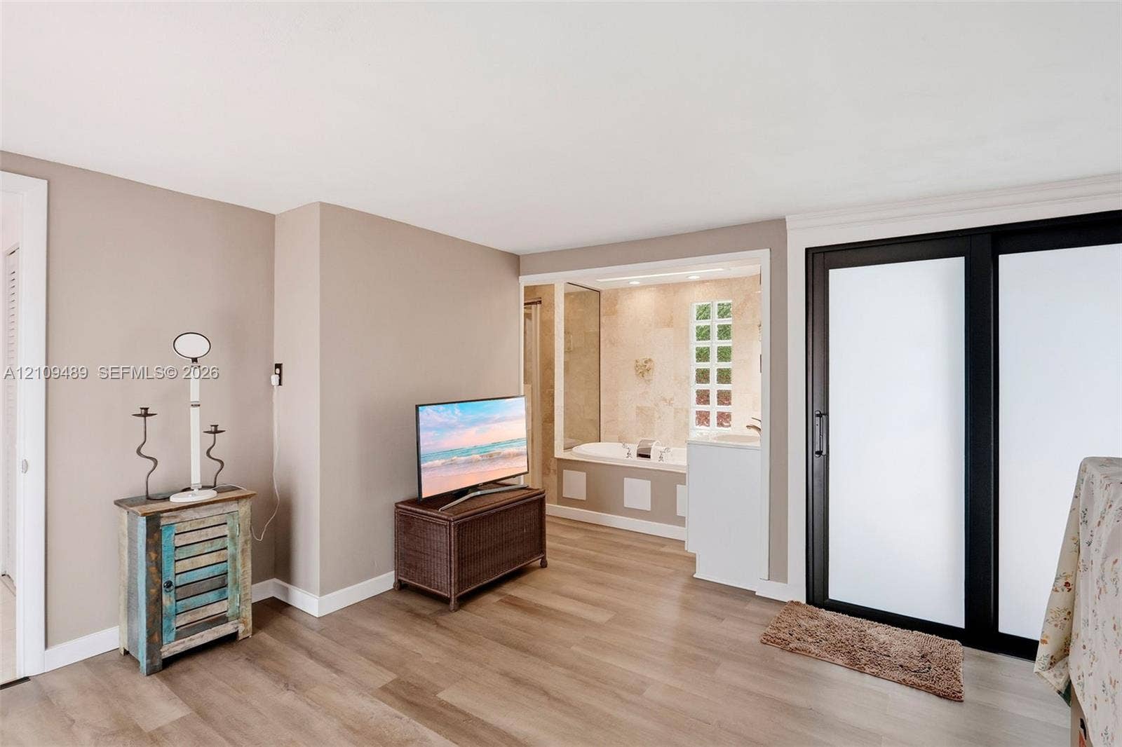 Fort Lauderdale, FL 33312 Neutral-toned interior featuring wood-finish flooring, sliding glass doors with dark frames, and a soaking tub alcove accented with natural stone-finish wall tile