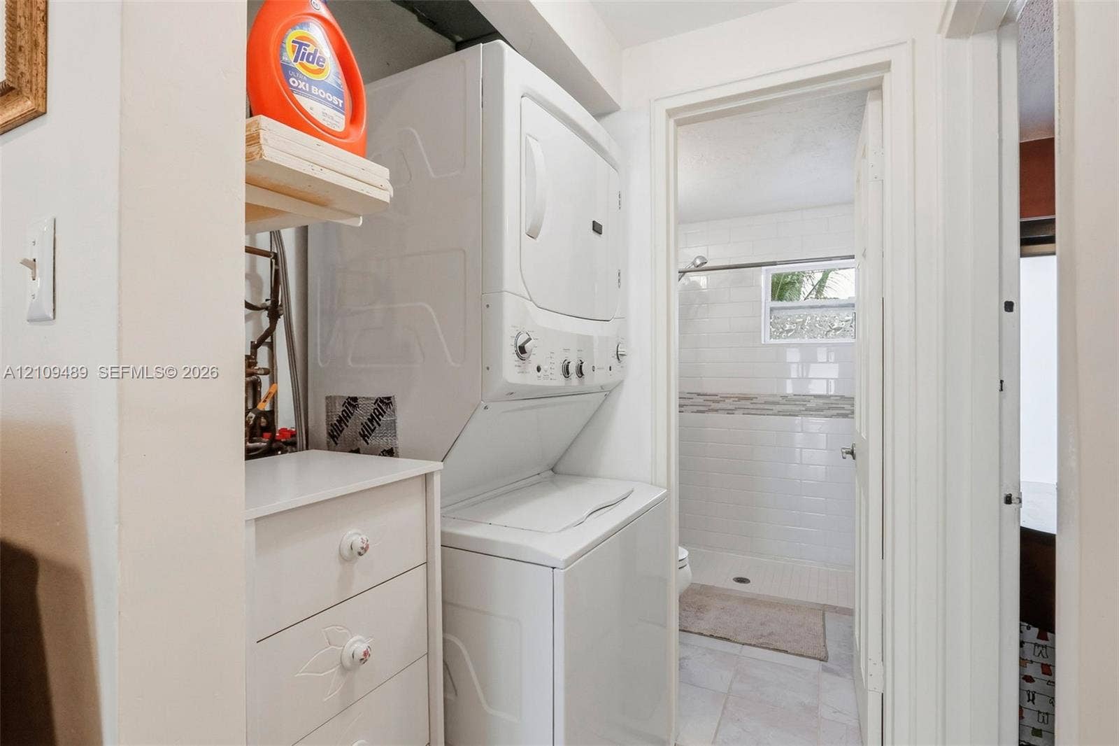 Fort Lauderdale, FL 33312 Stacked laundry unit with built-in storage cabinetry, white tile bathroom flooring, subway tile shower surround, and a framed window