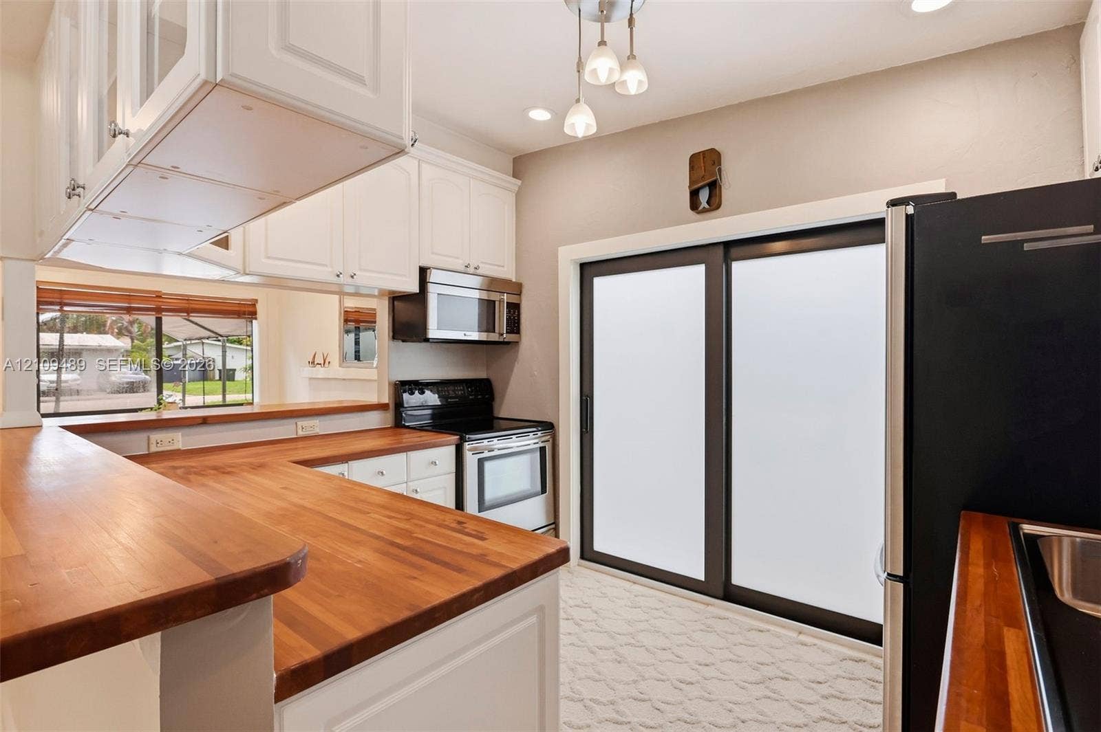 Fort Lauderdale, FL 33312 Kitchen featuring white cabinetry, butcher-block countertops, stainless steel appliances, a multi-light pendant fixture, and sliding glass doors