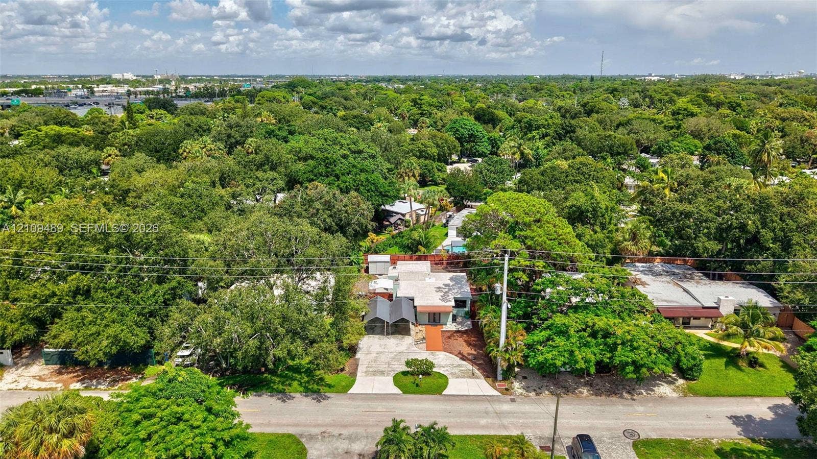 Fort Lauderdale, FL 33312 Aerial perspective featuring a single-story residence with a paved driveway, metal-framed carport, and mature tree canopy throughout the lot