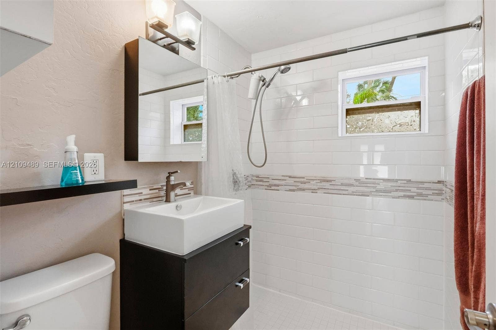 Fort Lauderdale, FL 33312 Modern vanity featuring a rectangular vessel sink and matte finish cabinetry, paired with a subway-tiled shower surround accented by a decorative glass mosaic border and a polished metal hand-held shower fixture