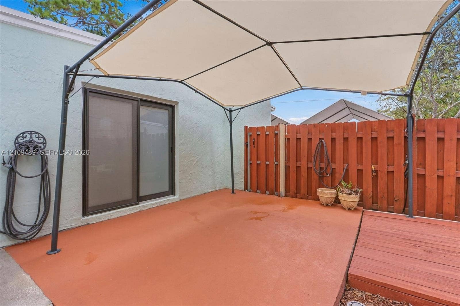 Fort Lauderdale, FL 33312 Exterior patio featuring a concrete surface, sliding glass door, wooden privacy fencing, and a metal-frame canopy
