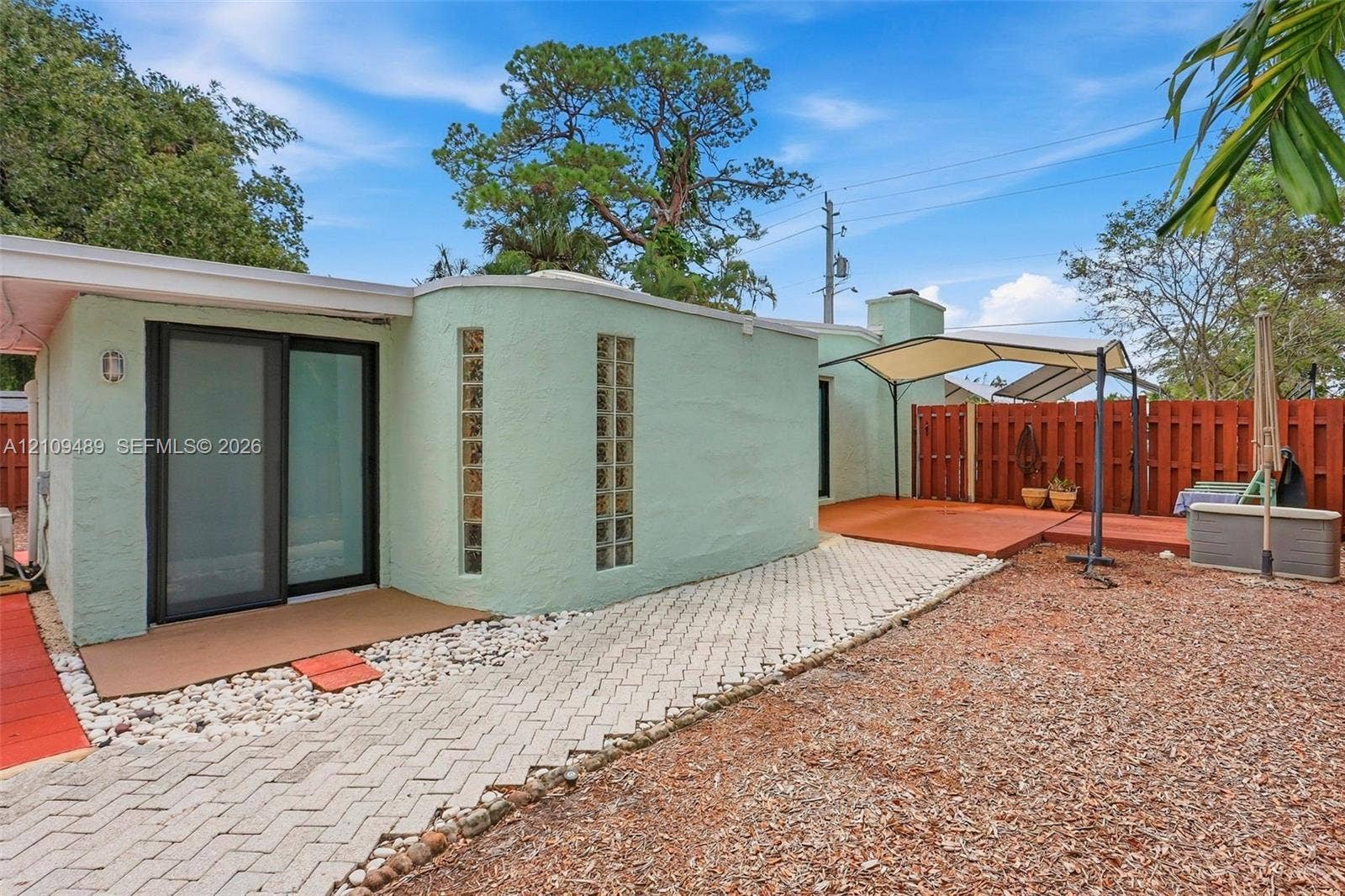 Fort Lauderdale, FL 33312 Stucco exterior featuring vertical glass block accents, a sliding glass door, a paved stone pathway, and wood-finish decking