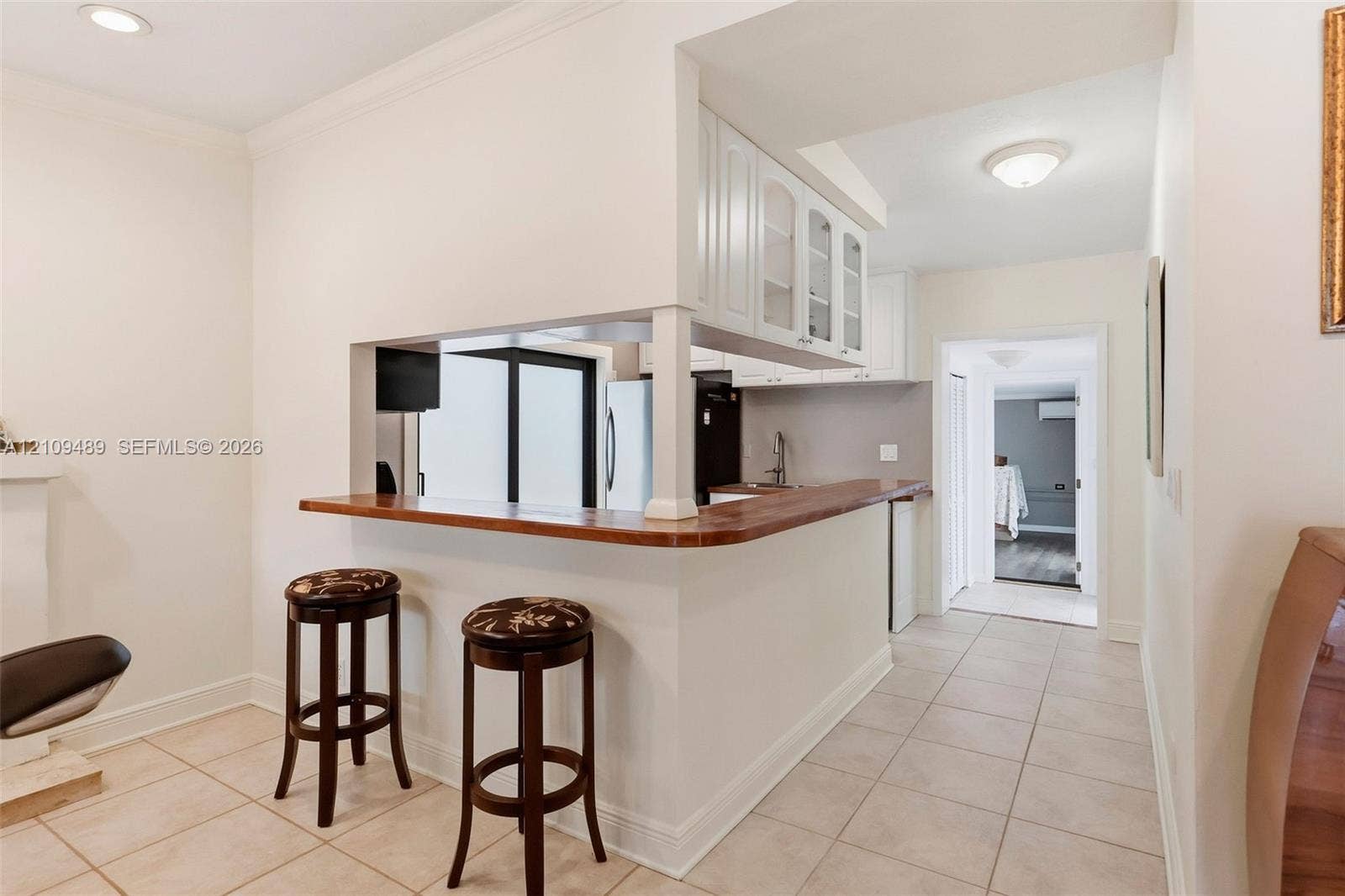 Fort Lauderdale, FL 33312 Pass-through kitchen counter with wood surface, white cabinetry with glass-front uppers, and neutral tile flooring