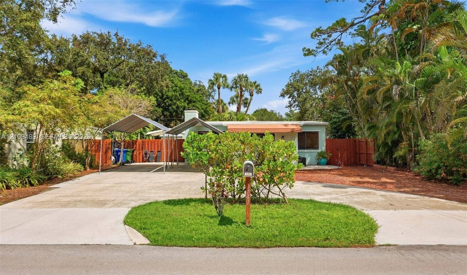 Fort Lauderdale, FL 33312 Exterior featuring a concrete driveway, dual metal carports, a landscaped front lawn, and wood privacy fencing