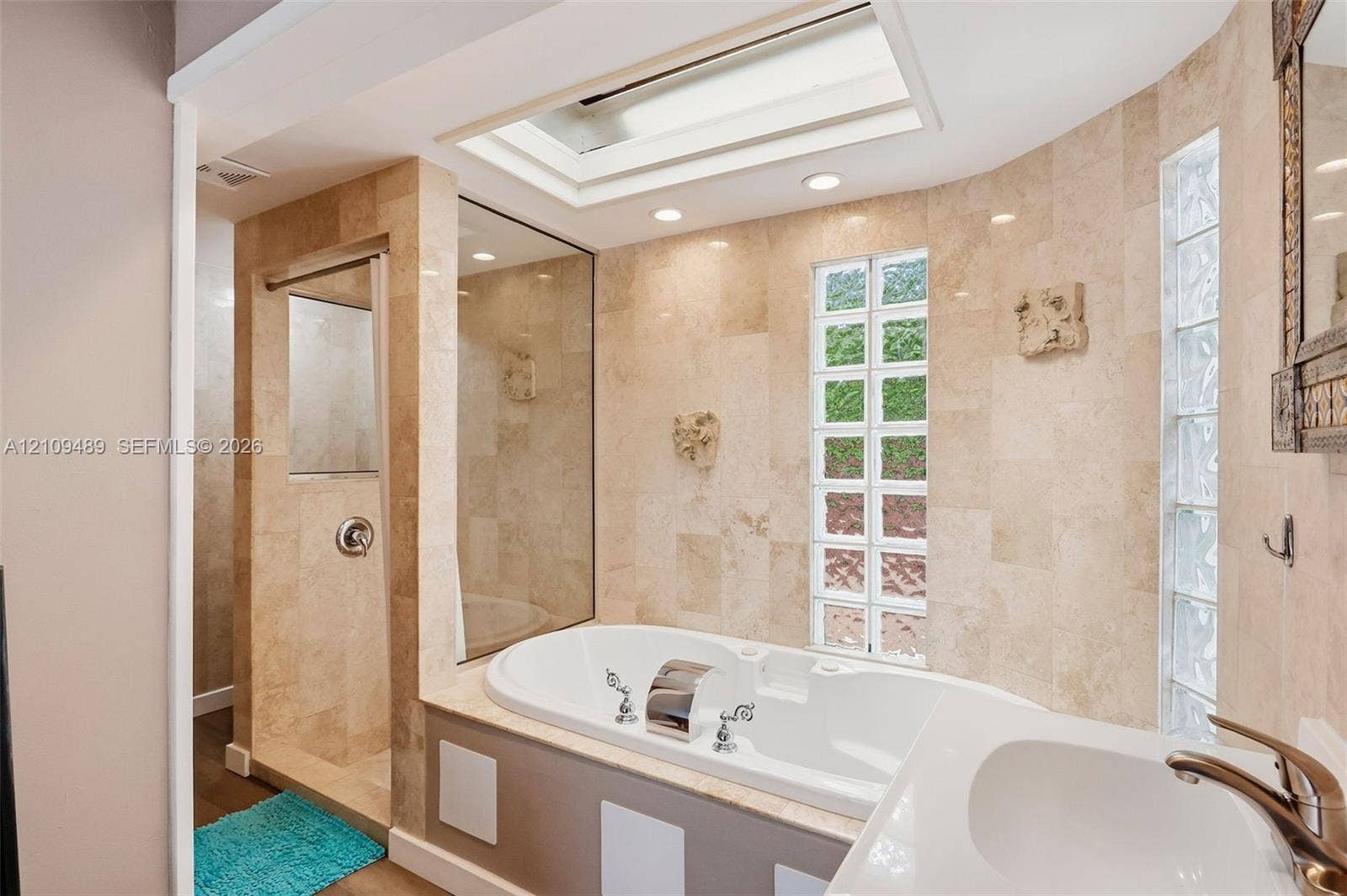 Fort Lauderdale, FL 33312 Bathroom featuring a drop-in soaking tub, tile-surround shower with a glass partition, dual glass-block windows, and a built-in skylight