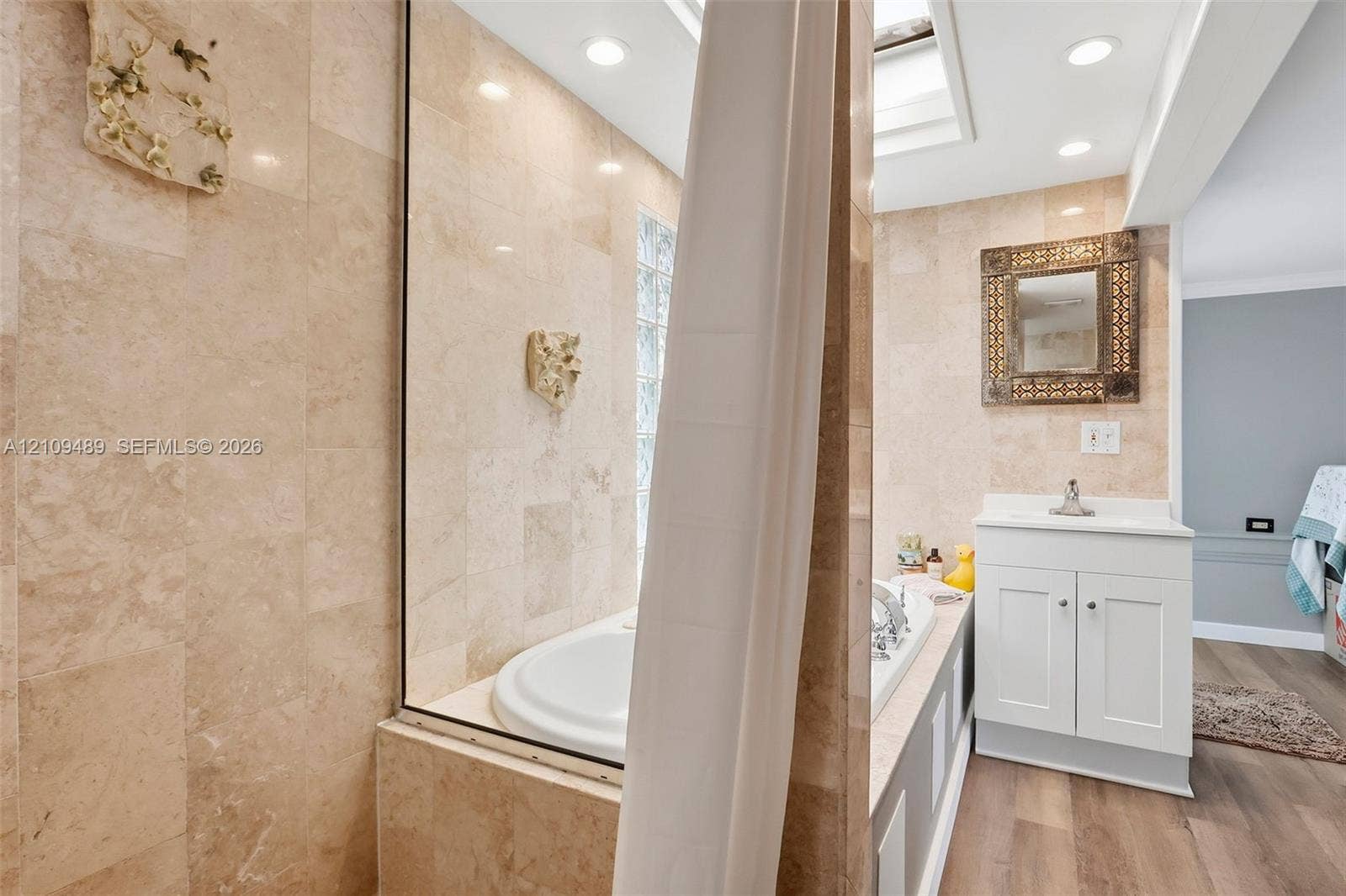 Fort Lauderdale, FL 33312 Bathroom featuring stone tile walls, a built-in soaking tub, a skylight, wood-finish flooring, and a white vanity cabinet