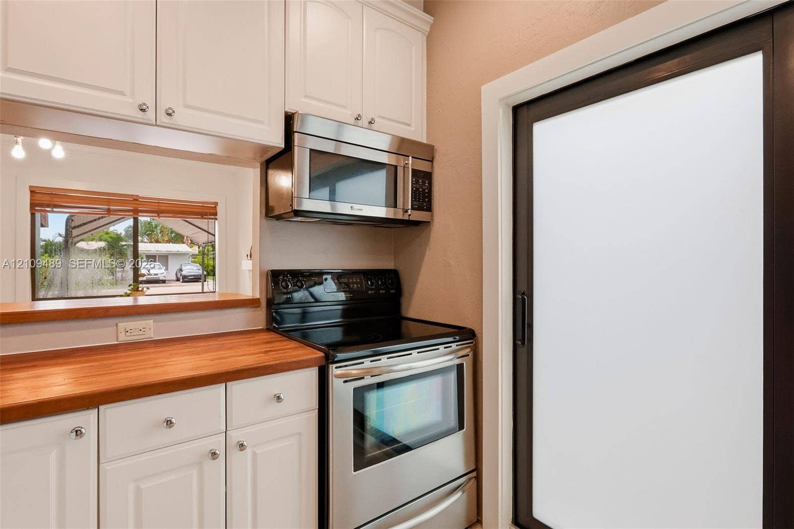 Fort Lauderdale, FL 33312 Kitchen featuring white shaker-style cabinetry, stainless steel microwave, black electric range, wood countertop, and a sliding glass door with a dark frame