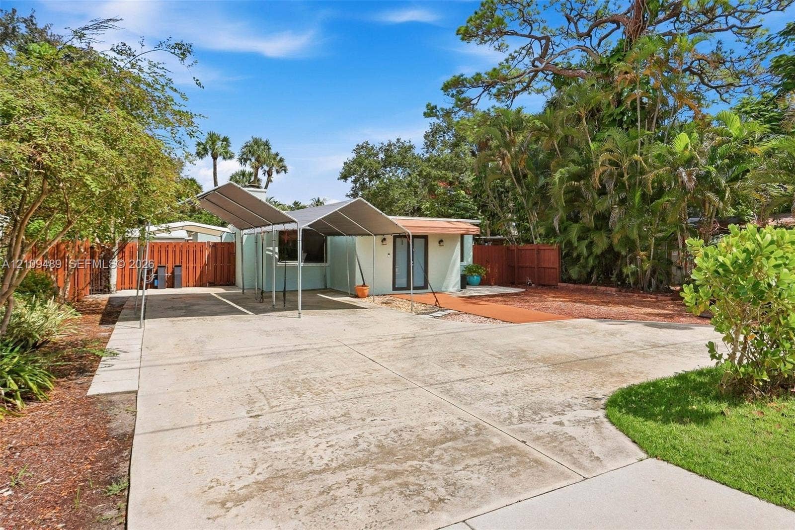 Fort Lauderdale, FL 33312 Exterior space featuring a concrete driveway, metal-framed carport, fenced perimeter, and mature landscape