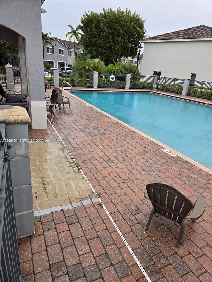 Rectangular swimming pool featuring brick paver decking, decorative metal fencing, and stone-capped perimeter pillars