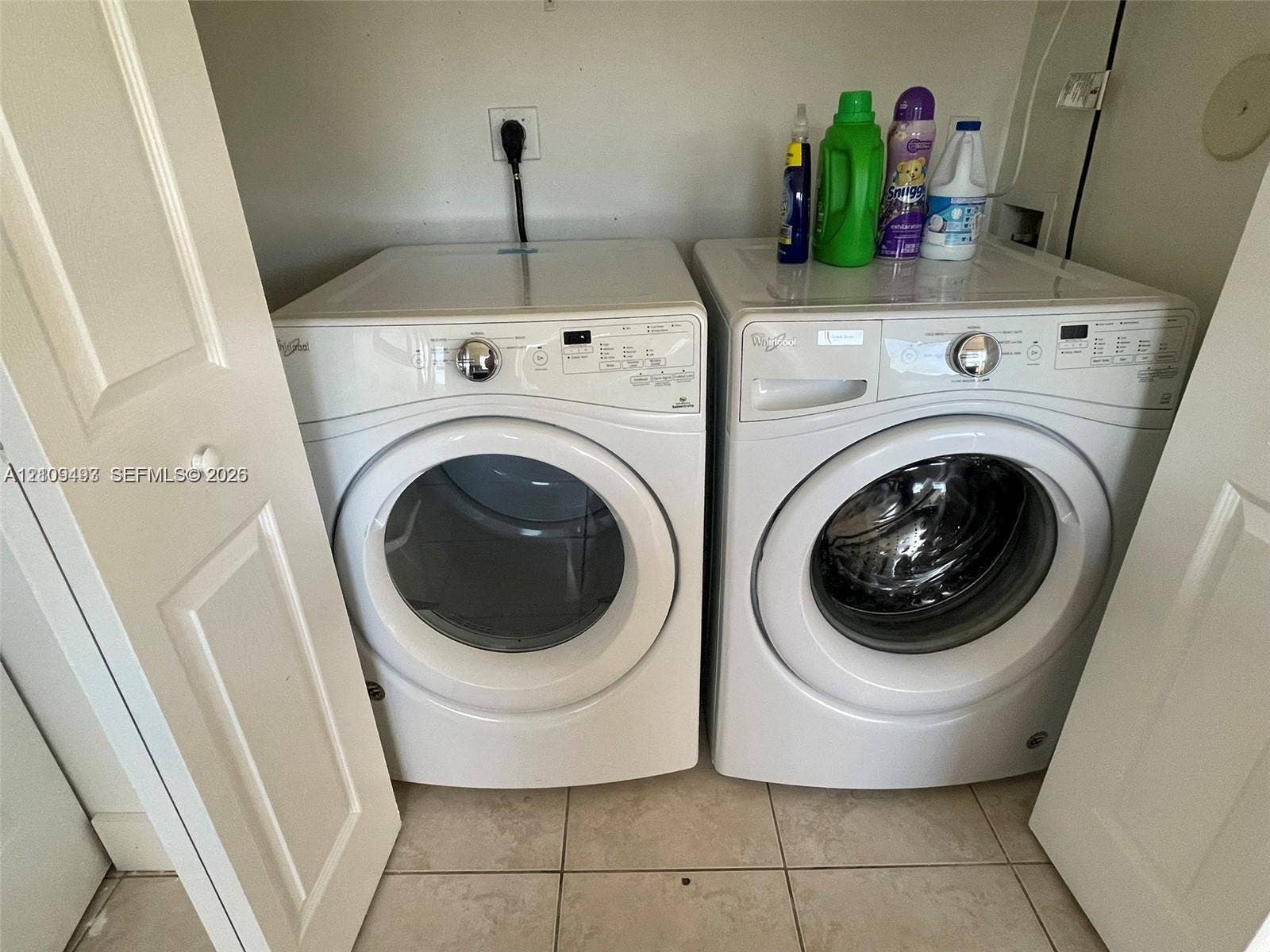 Laundry closet featuring dual white front-load appliances and neutral floor tiling
