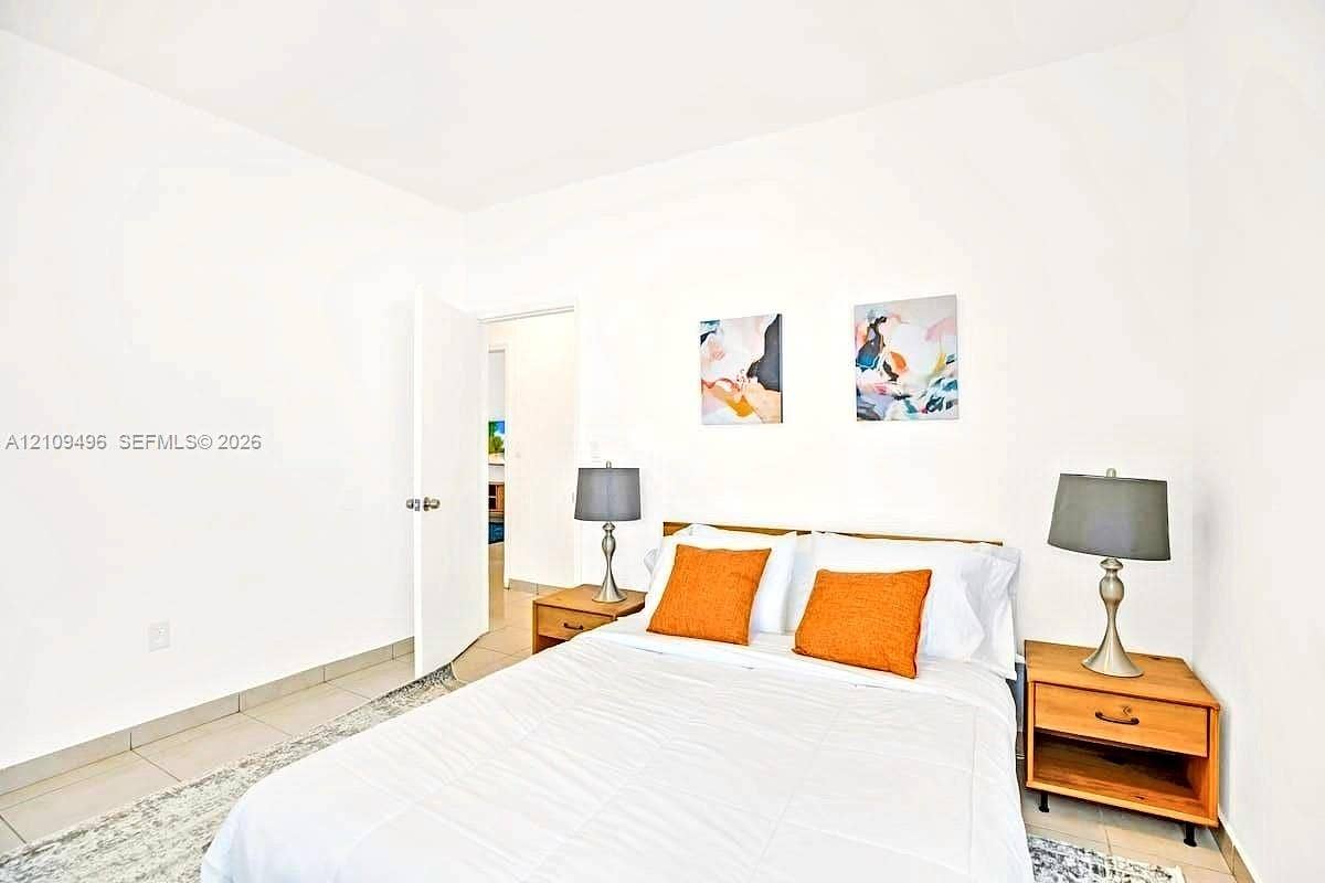 Neutral-toned ceramic tile flooring throughout, featuring a clean, minimalist interior aesthetic with white walls and a white swing door