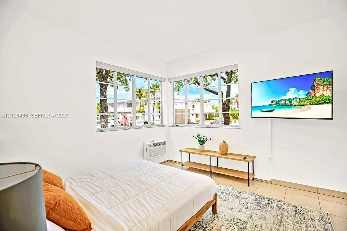 Corner room featuring large paneled windows, neutral wall-to-wall tile flooring, and a wall-mounted unit for climate control