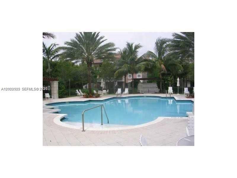 6804 W Sample Road, #6804, Coral Springs, Coral Springs, FL 33067 In-ground swimming pool featuring a curved design, metal handrail, concrete paver decking, and surrounding mature palm trees