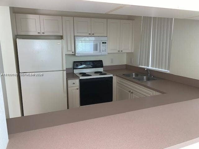 6804 W Sample Road, #6804, Coral Springs, Coral Springs, FL 33067 Kitchen featuring white cabinetry, solid-surface countertops, dual-basin sink, and white appliances including a built-in microwave and range