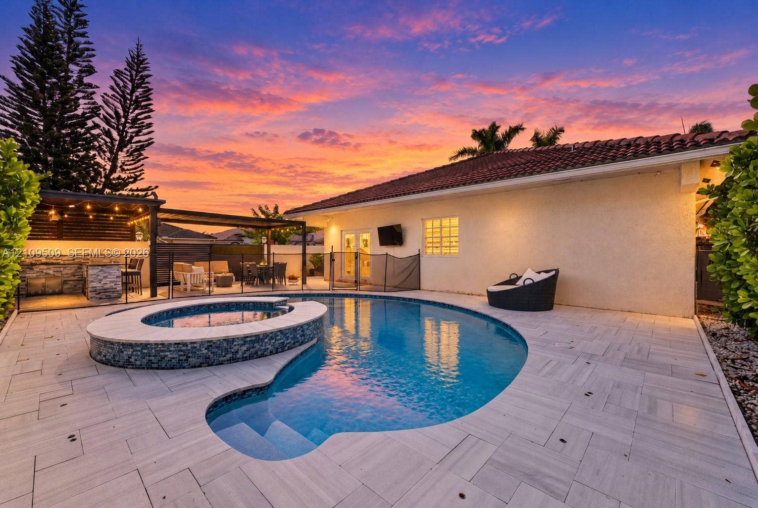 7721 NW 201st Terrace, Hialeah, FL 33015 Custom pool with integrated spa featuring mosaic tile detailing, expansive stone-paver patio, and covered outdoor kitchen structure