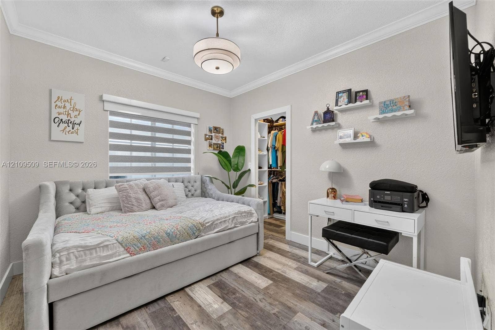 7721 NW 201st Terrace, Hialeah, FL 33015 Neutral-toned room featuring wood-finish flooring, crown molding, tiered pendant lighting, a window with roller shades, and a built-in walk-in closet